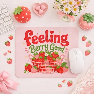 Peut inclure: Un tapis de souris rose avec le texte "Feeling Berry Good" et un panier de fraises. L'image comprend également une souris blanche, des décorations sur le thème des fraises et un clavier.