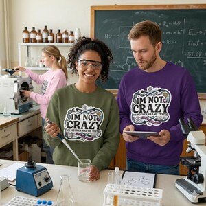 Puede incluir: Una mujer con una sudadera verde y un hombre con una sudadera morada, ambos con el texto "I'M NOT CRAZY MY MOTHER HAD ME TESTED". Las sudaderas están en un laboratorio.