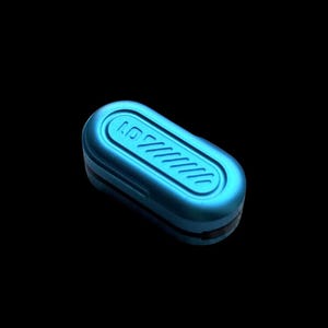 Può includere: Una piccola custodia di colore blu metallizzato, di forma ovale e con una finitura opaca liscia. La superficie superiore presenta un'area ovale allungata e incassata contenente una serie di scanalature diagonali parallele. La custodia ha una cucitura.