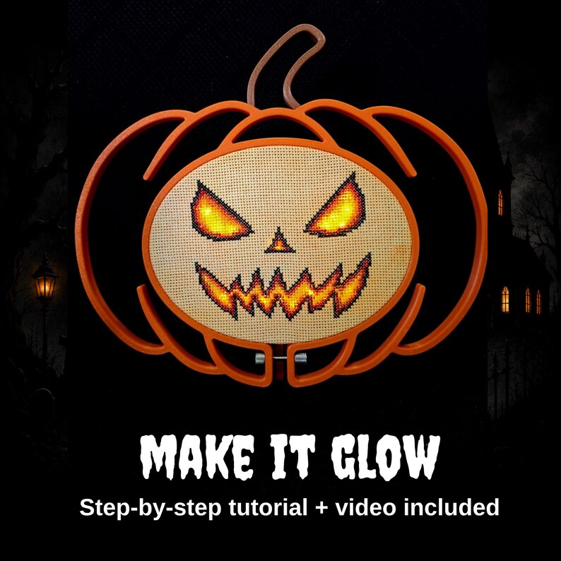 May include: An orange pumpkin-shaped embroidery hoop frame containing a cross-stitch design of a jack-o'-lantern face with glowing yellow and orange eyes and a jagged mouth. The text below reads MAKE IT GLOW Step-by-step tutorial + video included.