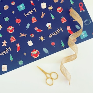 Peut inclure: Papier cadeau bleu marine avec un motif festif de pulls, de chaussettes et de cadeaux. Les mots "homey" et "snuggly" sont écrits sur le papier. Une paire de ciseaux dorés et un ruban de jute sont également présents.