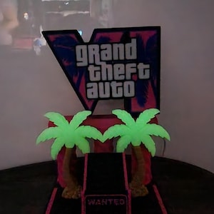 Pode incluir: Um expositor decorativo com o logótipo Grand Theft Auto V em texto branco sobre um fundo rosa e roxo. Duas palmeiras verde-claras estão à frente do logótipo, com uma base retangular preta com a inscrição Wanted em letras vermelhas.