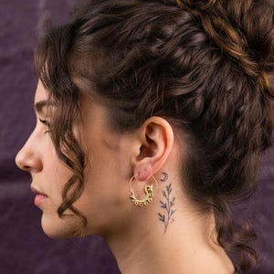 May include: A gold hoop earring featuring a series of small, circular beads along the outer edge. The earring is worn in the earlobe, showcasing a circular wire design with a textured, beaded finish that creates a distinct, metallic appearance.