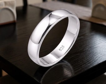May include: A shiny silver ring with a rounded band. The ring is stamped with "925" on the inside, indicating its silver content. The ring is displayed on a dark surface, reflecting the light and highlighting its polished finish.