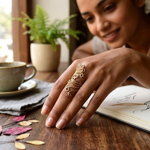 May include: A gold-toned metal ring featuring an elongated, openwork design with intricate swirling filigree patterns that extend vertically along the finger, showcasing a delicate, interconnected wire structure with a polished metallic finish.