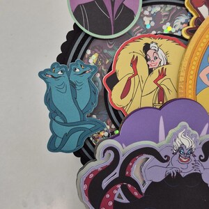 May include: A layered paper craft featuring cartoon villains. Includes Maleficent, Cruella de Vil, Ursula, and others. The characters are in various colors, with a black and purple theme. The craft has a circular shape.