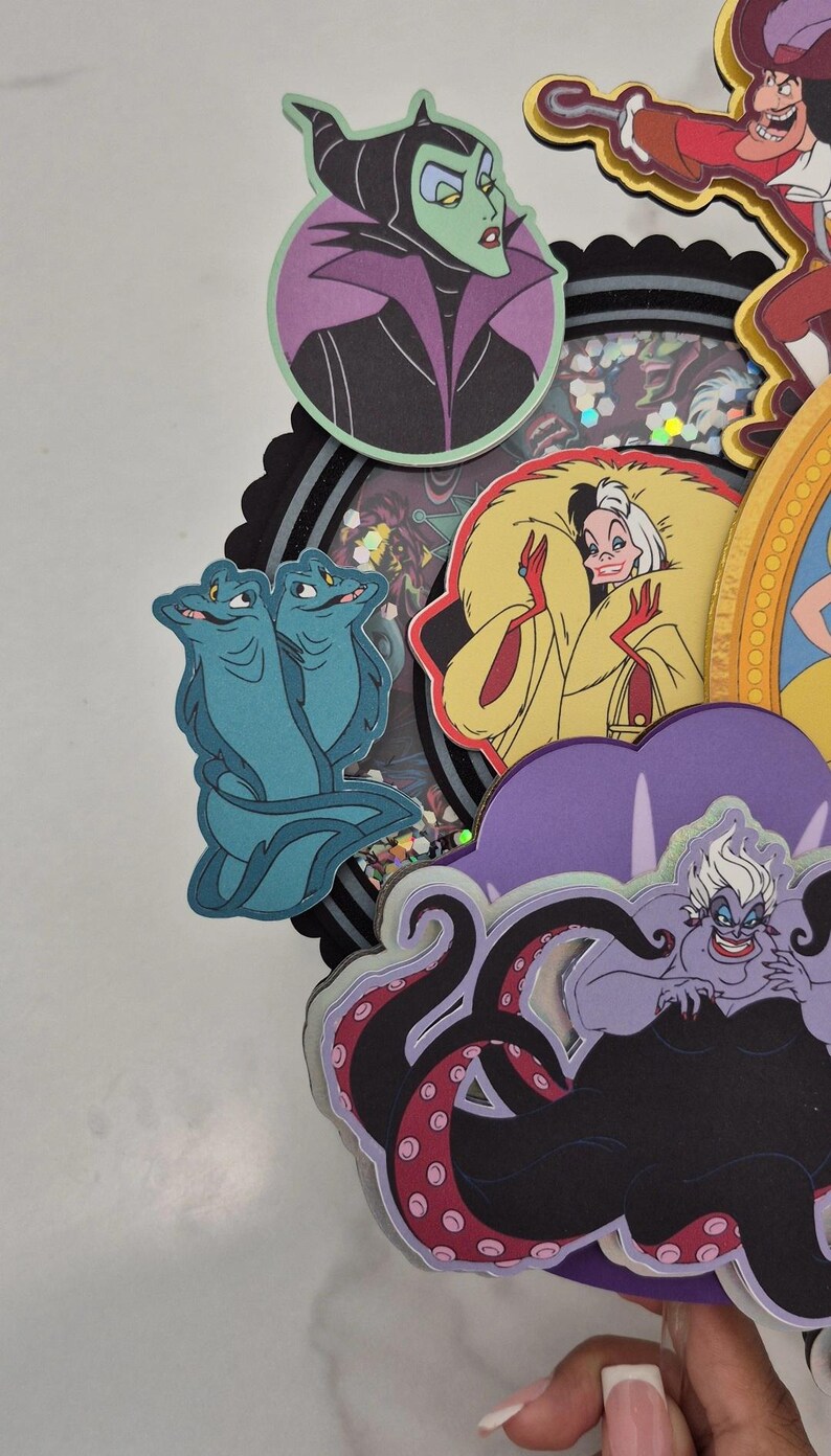May include: A layered paper craft featuring cartoon villains. Includes Maleficent, Cruella de Vil, Ursula, and others. The characters are in various colors, with a black and purple theme. The craft has a circular shape.