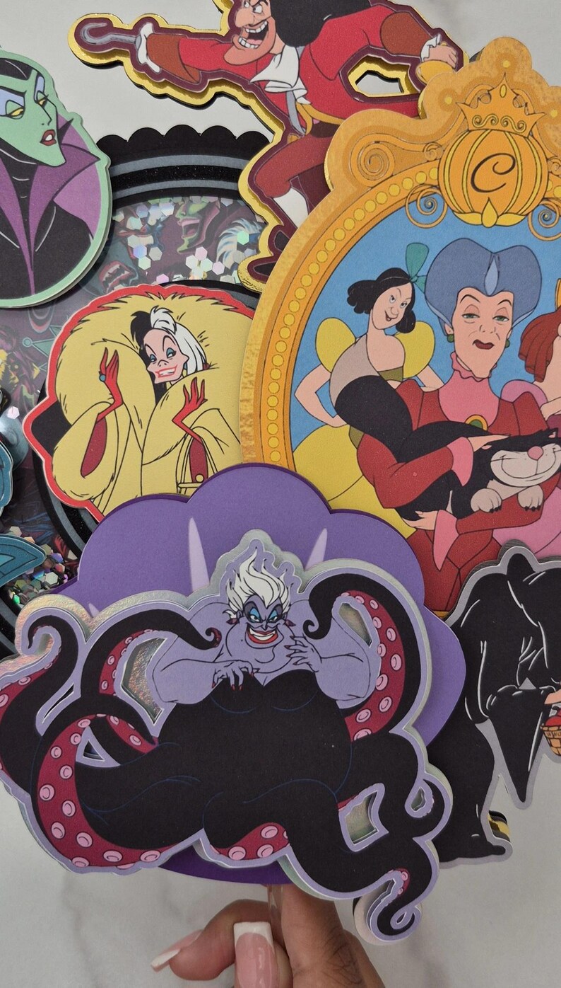 May include: A collection of colorful, layered paper cutouts featuring Disney villains and characters. Includes Ursula, Cruella de Vil, Captain Hook, and Cinderella's stepmother. The cutouts have a glittery, iridescent background.