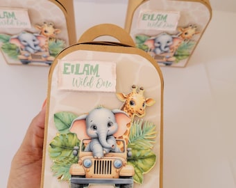 May include: Three brown cardboard gift boxes with handles. Each box features a safari theme with an elephant in a jeep and a giraffe. The text "EILAM Wild One" is printed on a label on the front of each box.
