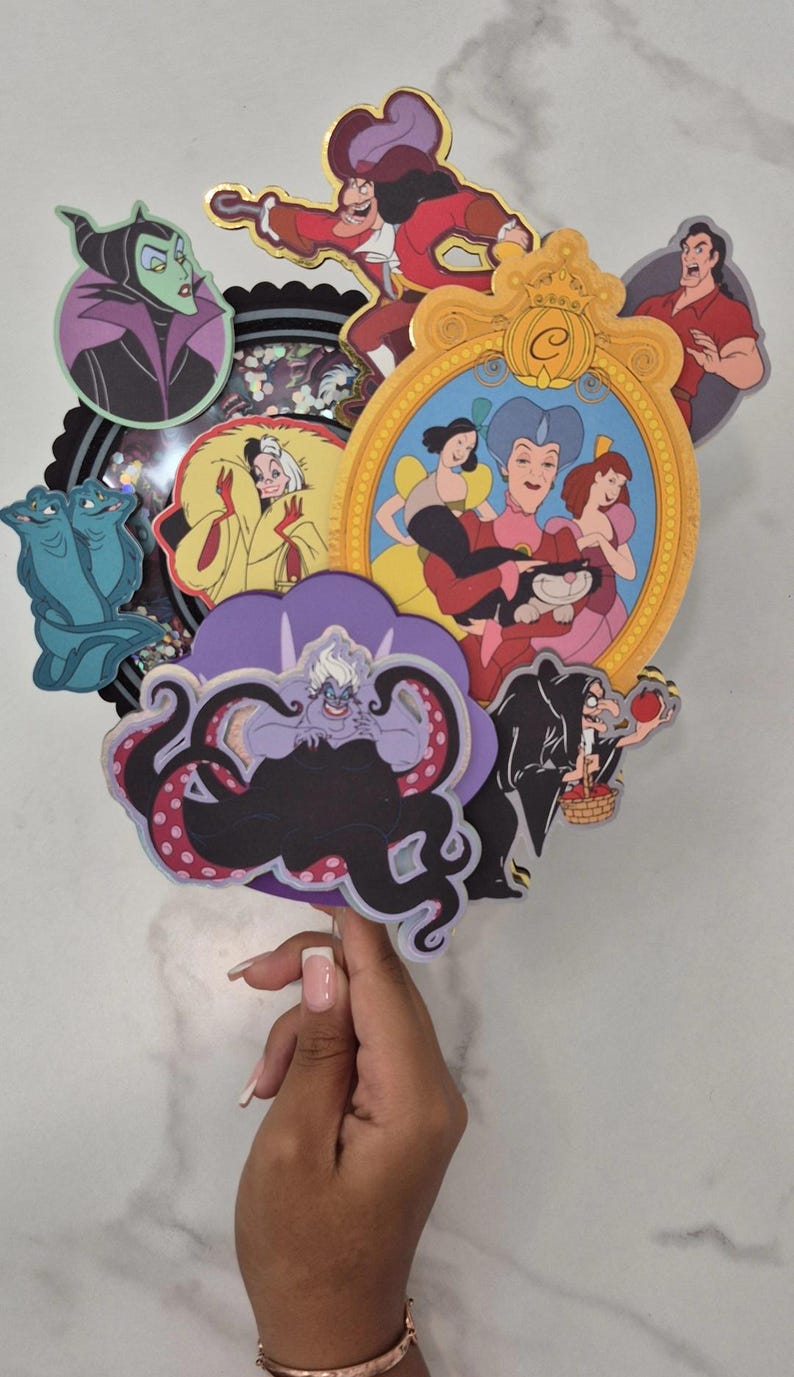 May include: A collection of colorful cartoon character cutouts, including Ursula, Maleficent, and Captain Hook. The characters are arranged in a layered design, with a gold-framed image of Cinderella and her stepfamily. The overall theme is Disney villains.