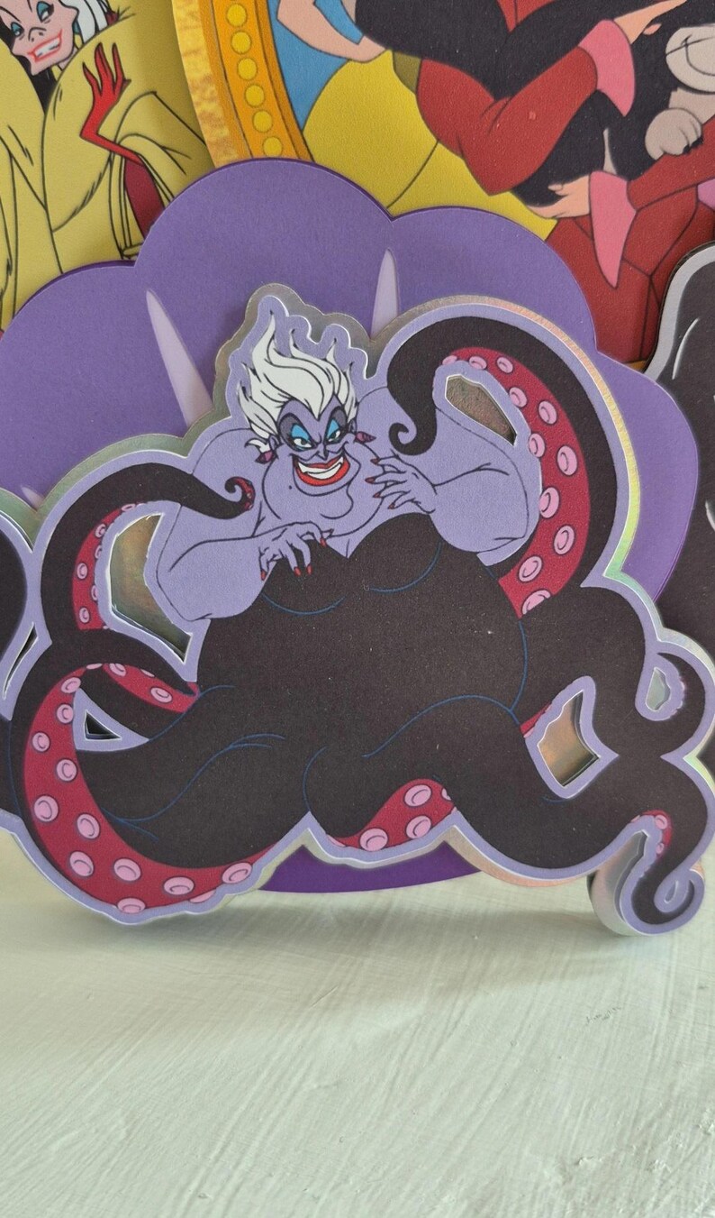 May include: A purple Ursula the Sea Witch character cutout with white hair, red lipstick, and black tentacles with pink spots. The cutout is surrounded by other cartoon character cutouts.