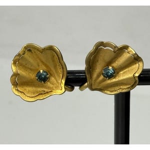 May include: A pair of gold-toned metal clip-on earrings shaped like stylised, ruffled flower petals. Each earring features a single, small, round, dark blue gemstone set securely in the centre of the textured, scalloped metal petal design.