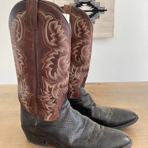 May include: A pair of brown leather cowboy boots with intricate stitching and a pointed toe. The boots are worn and have a distressed look.