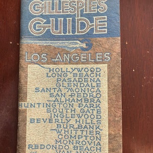 May include: A vintage guidebook cover for Gillespie's Guide to Los Angeles. The cover is blue and tan with the title in a large, bold font. The guidebook lists cities and towns in the Los Angeles area, including Hollywood, Long Beach, Pasadena, Glendale, Santa Monica, San Pedro, Alhambra, Huntington Park, South Gate, Inglewood, Beverly Hills, Burbank, Whittier, Compton, Monrovia, Redondo Beach, Van Nuys, and 74 other towns.