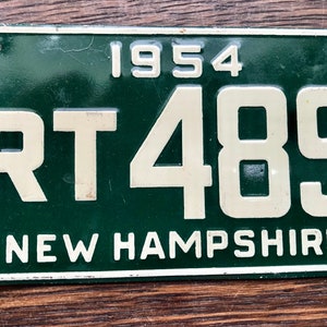 May include: Green metal license plate with white lettering. The plate reads "1954 RT 489 NEW HAMPSHIRE".