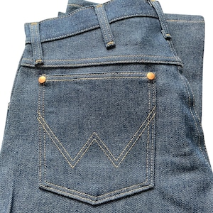 May include: Close-up of a pair of blue denim jeans. The jeans feature a classic five-pocket design with a back pocket showcasing a distinctive 'W' stitch pattern. The jeans have copper-colored rivets and tan stitching.
