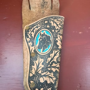 Könnte beinhalten: Ein braunes Lederholster mit einem schwarzen und weißen Blumendesign und einem blauen Pferdekopf-Emblem.