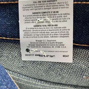 May include: Close-up of a tag attached to denim fabric. The tag includes text in English, French, and Spanish, detailing a one-year warranty. The tag also includes the Wrangler Q.C. Department address.