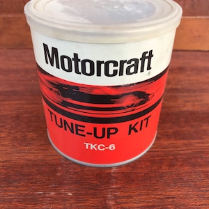 May include: A red and white cylindrical can with the text "Motorcraft" in black lettering. The can has a black and red graphic design and the text "TUNE-UP KIT" in black lettering. The text "TKC-6" is printed in black lettering on the bottom of the can.