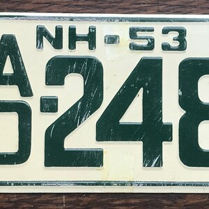 May include: Vintage New Hampshire license plate with the state abbreviation "NH" and the number "53" at the top. The plate displays the numbers "0 248" in dark green against a cream background. The plate has two holes for mounting.