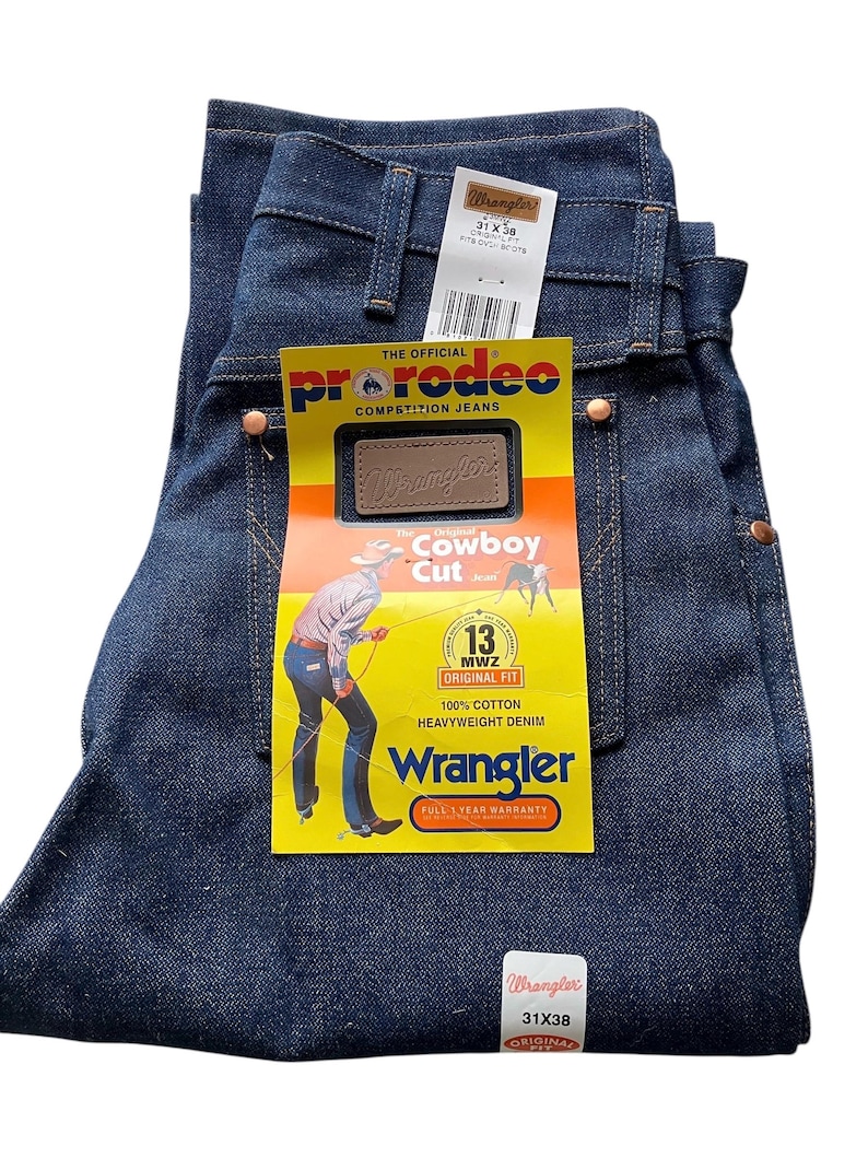 May include: Dark blue Wrangler Cowboy Cut jeans, size 31x38, with tags. The jeans have copper rivets and a yellow tag with a cowboy illustration. The tag reads "100% Cotton Heavyweight Denim."