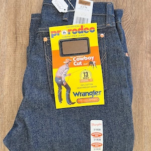 May include: Dark blue Wrangler Cowboy Cut jeans, size 31x38, with tags. The jeans have copper rivets and a yellow tag with a cowboy illustration. The tag reads "Pro Rodeo Competition Jeans" and "Original Cowboy Cut".