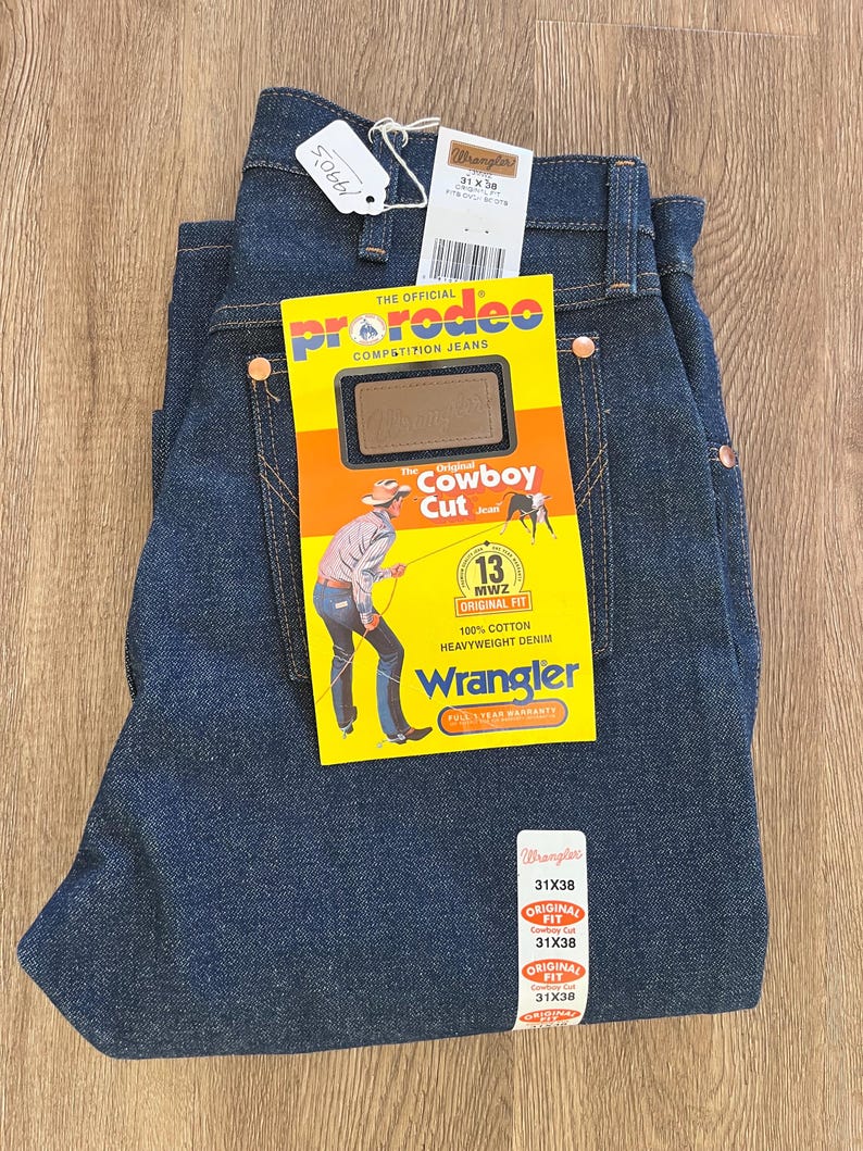 May include: Dark blue Wrangler Cowboy Cut jeans, size 31x38, with tags. The jeans have copper rivets and a yellow tag with a cowboy illustration. The tag reads "Pro Rodeo Competition Jeans" and "Original Cowboy Cut".
