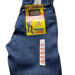 May include: Dark blue Wrangler ProRodeo Cowboy Cut jeans with tags. The jeans have a classic fit and are made of 100% heavyweight denim. The tags display the Wrangler logo and the size 31x38.