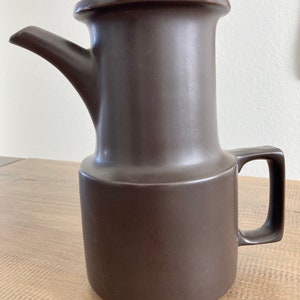 May include: A brown ceramic pitcher with a wide spout and a handle. The pitcher has a cylindrical shape with a slightly flared top.
