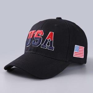 May include: Black baseball cap with the word "USA" embroidered in red, white, and blue. The cap features a small American flag patch on the side. A classic, patriotic accessory.