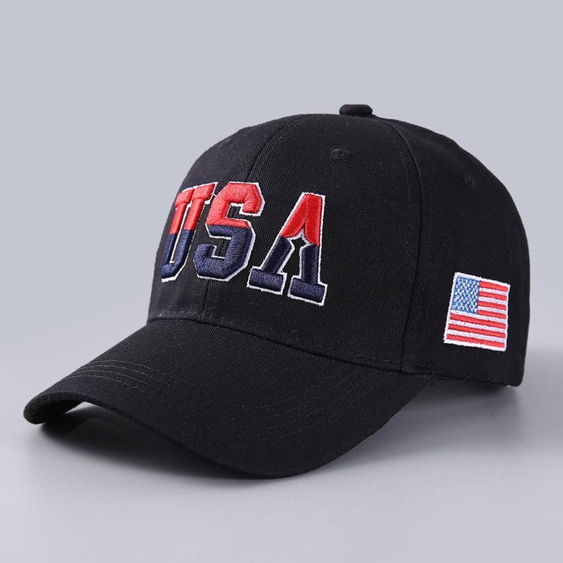 May include: Black baseball cap with the word "USA" embroidered in red, white, and blue. The cap features a small American flag patch on the side. A classic, patriotic accessory.