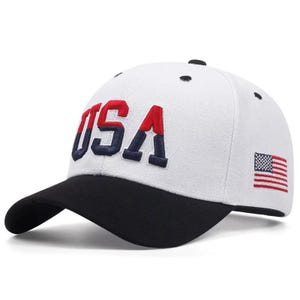 May include: White baseball cap with a black brim, featuring the embroidered word "USA" in red and navy blue. The American flag is embroidered on the side. A stylish accessory for casual wear.