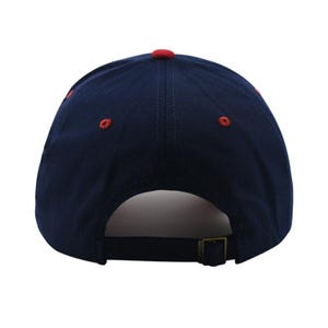 May include: A navy blue baseball cap with a red button on top and red stitching details. The cap has a curved brim and an adjustable metal buckle closure at the back. The hat is made of a durable fabric.