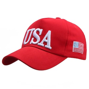 Puede incluir: Gorra de b&eacute;isbol roja con la palabra "USA" bordada en blanco en la parte delantera. La gorra tiene una visera curva y una bandera americana bordada en el lateral.