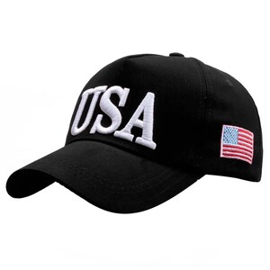 Puede incluir: Gorra de b&eacute;isbol negra con la palabra "USA" bordada en blanco en la parte delantera. Un peque&ntilde;o parche de la bandera estadounidense est&aacute; en el lateral. La gorra tiene una visera curva y un bot&oacute;n en la parte superior.