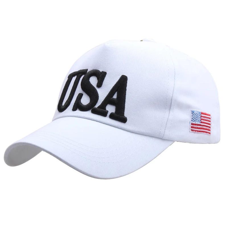 Puede incluir: Gorra de b&eacute;isbol blanca con la palabra "USA" en letras negras bordadas en la parte delantera. Una peque&ntilde;a bandera americana bordada est&aacute; en el lateral. La gorra tiene una visera curva.