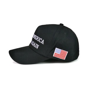 Puede incluir: Gorra de b&eacute;isbol negra con las palabras "AMERICA AGAIN" bordadas en blanco. Tiene un peque&ntilde;o parche de la bandera estadounidense en el lateral. La gorra tiene una visera curva y un bot&oacute;n en la parte superior.
