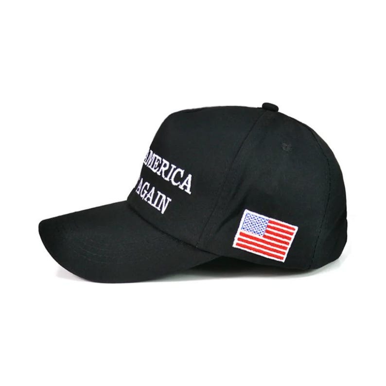 Puede incluir: Gorra de b&eacute;isbol negra con las palabras "AMERICA AGAIN" bordadas en blanco. Tiene un peque&ntilde;o parche de la bandera estadounidense en el lateral. La gorra tiene una visera curva y un bot&oacute;n en la parte superior.