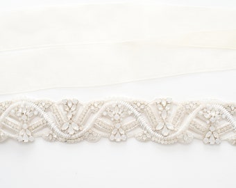 May include: A white beaded trim with a delicate, intricate design. The trim features small, clear rhinestones and pearls, creating a shimmering effect. This trim is perfect for adding a touch of elegance to any project.
