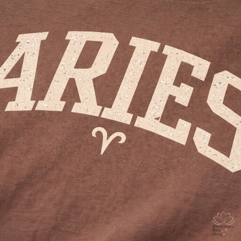 May include: Close-up of a brown fabric with the word "ARIES" in a distressed, off-white font. Below the word is the Aries zodiac symbol. The image has a vintage, textured look.