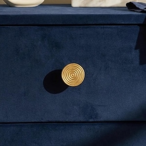 May include: Close-up of a navy blue velvet drawer with a gold spiral knob. The knob is centered on the drawer, casting a shadow. The drawer is part of a larger piece of furniture.
