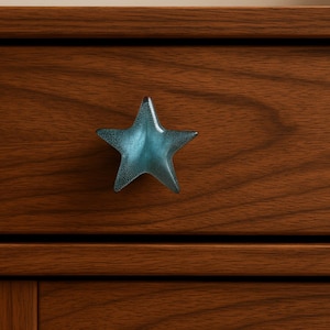 May include: A blue star-shaped cabinet knob with a textured surface. The knob is mounted on a wooden drawer with a rich brown finish. The star has a translucent appearance, adding a decorative touch to the furniture.