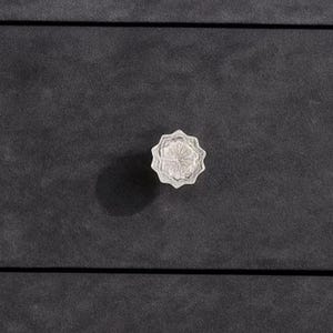 Puede incluir: Primer plano de un pomo de cristal transparente, facetado y con diseño de estrella. El pomo está montado sobre una superficie gris oscuro, probablemente un cajón o puerta de armario. El pomo es un elemento decorativo.