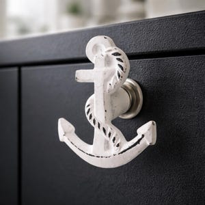 May include: White anchor-shaped cabinet knob with a distressed finish, mounted on a black cabinet door. The nautical-themed hardware features a rope detail and a silver-toned base.