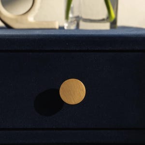 May include: A close-up of a navy blue velvet drawer with a round, light wood knob. The knob casts a shadow on the drawer. The image suggests a piece of furniture, possibly a dresser or nightstand.
