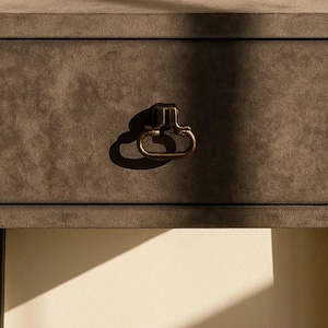 May include: Close-up of a dark gray drawer with a bronze-colored handle. The drawer has a textured surface and is part of a larger piece of furniture. The handle is a classic, curved design.