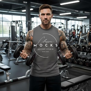 May include: A gray sleeveless shirt with the text "Classic Mocks Mockup Studio Estd 2023" in a white circular design. The person is holding two black dumbbells in a gym setting.
