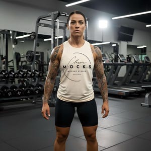 May include: A person wearing a cream-colored tank top with the text "Classic Mocks Mockup Studio" in a gym setting. The person is also wearing black shorts. Dumbbells and exercise equipment are visible in the background.