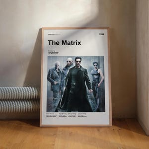 Peut inclure: Une affiche encadrée du film "The Matrix" de 1999, représentant les acteurs. L'affiche a un bord blanc et est posée contre un mur. Le titre "The Matrix" est en gras, en noir.
