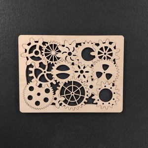 Può includere: Targa rettangolare in legno chiaro con un design di ingranaggi intagliati in modo intricato di varie dimensioni. Gli ingranaggi sono disposti all'interno di una cornice, creando un'estetica meccanica o steampunk. Sfondo scuro.